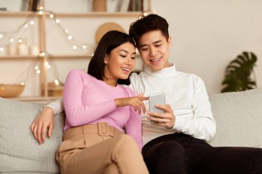 Çinli bir çift hafta sonu akıllı telefon kullanıyor. Evde koltukta oturup, akşamları birlikte geçiriyorlar. Mobil Uygulama, Telefon Kullanıcıları İnternet Taraması, Gadget Yaşam Tarzı Konsepti