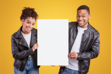 Sarı Stüdyo Arkaplanı 'nın üzerinde duran, siyah deri ceketli, gülümseyen, fotokopi için boş yer gösteren neşeli Afrikalı Amerikalı çift. Reklam Afişi