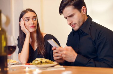 Bad Date. Unhappy Sad Beautiful Woman Is Getting Bored Sitting On Date Event In Restaurant While Her Boyfriend Using Mobile Phone And Chatting, Ignoring His Girlfriend. Relationship Problem Concept