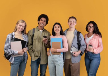 Farklı ülkelerden modern öğrenciler ve değişim programı. Sırtında kahve, kitap ve sırt çantalarıyla gülümseyen uluslararası genç insanlar, turuncu arka planda izole edilmiş kameraya bakıyorlar.