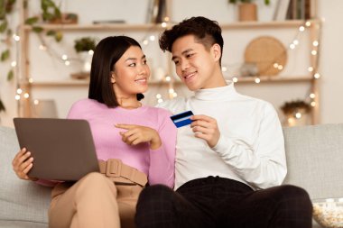 İnternetten bilgisayar ve kredi kartıyla alışveriş yapan mutlu Asyalı çift hafta sonları evdeki koltukta oturup internetten bir şeyler sipariş ediyor. Mutlu Müşteriler, Alışveriş ve E-Ticaret Konsepti