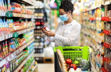 Zenci Kadın, marketten alışveriş yapan gıda ürünlerinin son kullanma tarihini kontrol ediyor. Alışveriş arabasıyla koridorda duruyor. Bayan Alıcı Sağlıklı Yemek Konseptini Seçiyor