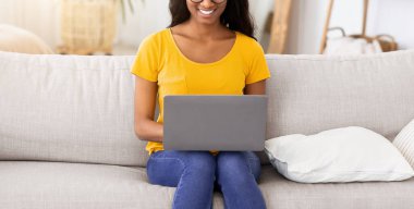 Neşeli siyah bayan rahat koltukta dizüstü bilgisayarıyla oturuyor ve evdeki arkadaşıyla iletişim kuruyor. Neşeli Afrikalı Amerikalı kadın çevrimiçi eğitim veya eğlence videosu izliyor, blogunda yayınlıyor.