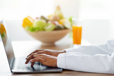Sağlıklı beslenme konsepti. Dizüstü bilgisayarda yazan zayıflama danışmanı klinikteki hastaya online danışmanlık yapıyor. Tıp bürosunda polisle çalışan dietolojistin yan görünüşü
