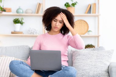 Hastalığın ilk belirtileri, migren, kendini izole ederken aşırı çalışma. Üzgün, genç, Afro-Amerikalı bir kadın dizüstü bilgisayarla koltukta oturuyor, alnına baskı yapıyor, oturma odasında baş ağrısından muzdarip.