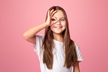 Her şey yolunda. Gülümseyen çocuk el pençe divan duruyor, parmaklarının arasından bakıyor, pembe arka planda izole edilmiş, stüdyo çekimlerinde.