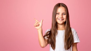 Uzun saçlı çocuk ürününü sunuyor. Mutlu küçük kız boş uzayda, pembe arka planda izole edilmiş, stüdyo çekimlerinde