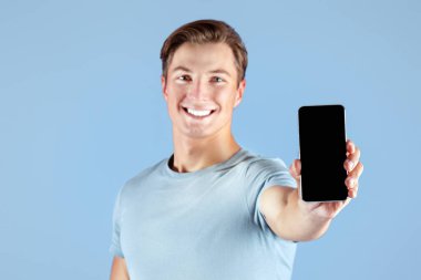 Leylak stüdyosunun arka planında boş ekranlı akıllı telefonu gösteren mutlu genç sporcu, mobil uygulama tasarımı için model. Güçlü milenyum adamı web sitesi şablonu için yeri olan cep telefonunu tutuyor