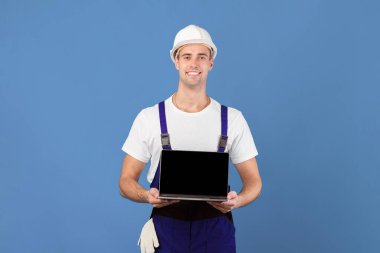 Sert Şapkalı Gülümseyen Ustabaşı Siyah Ekranlı Laptop, Yakışıklı İşçi Çevrimiçi İnşaat Aletleri Alışverişi İçin Yeni Web Sitesi Öneriyor, Mavi Arkaplanda Duruyor, Model Resim