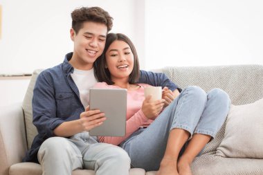 Evcil Asyalı çift, dijital tablet kullanıyor. Hafta sonu evde koltukta dinlenerek film seyrediyor. Sıcak bir tatil günü, Yurtiçi Yaşam Tarzı Kavramı. Boşluğu Kopyala