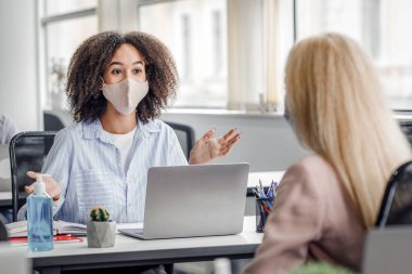 COVID-19 salgını sırasında müvekkil ile sosyal mesafe ve iletişim. Afrika kökenli Amerikalı yönetici, kadınlara iş yerinde dizüstü bilgisayar ve antiseptik içeren jestler ve kopyalama alanı öneriyor.