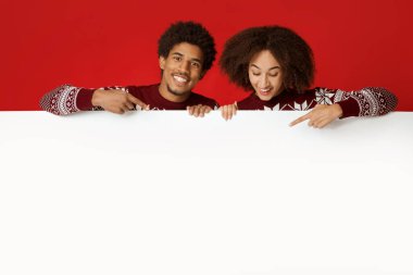 Birbirine aşık bir çift, yeni yıl ve Noel için harika bir öneri sunar. Mutlu Afro-Amerikan ailesi boş beyaz ilan panosuna bakıyor ve kırmızı arka planda izole edilmiş pankartı işaret ediyor.