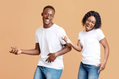 Joyful african american lovers having fun together, listening to music, moving and screaming over yellow studio background. Happy black man and woman enjoying time together, playing invisible guitars