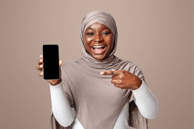 Kara Ekran ile Smartphone 'u işaret eden neşeli siyahi kadın, Tasarımınız için Kopya Alanlı Modern Gadget' ı gösteriyor, Işık Stüdyosu Arkaplanının Başında Duruyor, Model Resim