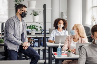 Yöneticiyle iş ve sosyal mesafe konusunda görüş alışverişi. Korunaklı maskeli bir kadın ve erkek, Coronavirus salgını sırasında iş yerinde konuşuyor.