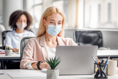 Müşteri desteği için yeni normal ve modern bir iş. Avrupalı ve Afrikalı Amerikalı yöneticiler, koronavirüs salgını sırasında antiseptikle birlikte iş yerlerinde dizüstü bilgisayarlar üzerinde çalışıyorlar.