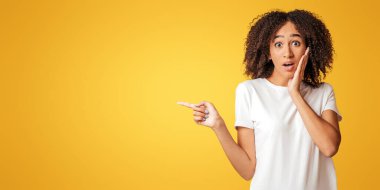 Büyük indirim, beklenmedik bir teklif ve inanılmaz bir reklam. Şaşırmış bin yıllık Afro-Amerikan kadını el ele tutuşuyor ve parmak boşluğa uzanıyor, sarı arka planda izole edilmiş, stüdyo çekimi