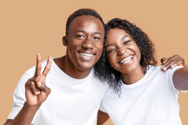 Neşeli Siyah Adam ve Kadın Selfie Çekiyor, gülümseyen adam zafer jesti yapıyor, sarı stüdyo geçmişi var, yakın plan. Mutlu Afro-Amerikan aşıkları mutlu anlarını arkadaşlarıyla paylaşıyor.