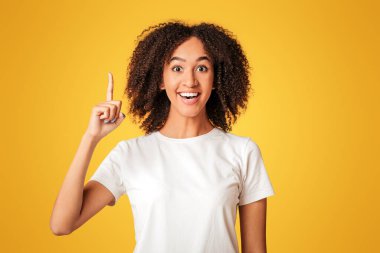 Harika bir fikir ve iyi bir ruh hali. Genç, zeki, Afro-Amerikalı bir kadın açık ağızlı, boş yeri işaret eden ve başarılı bir planı olan, turuncu arka planda, stüdyo çekiminde izole edilmiş,