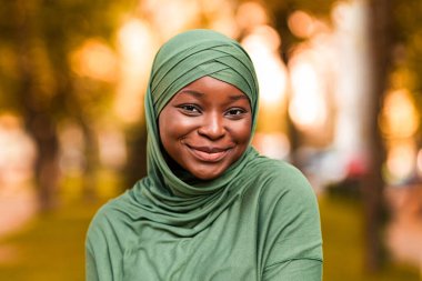 Modern tevazu. Açık havada tesettürlü, utangaç, siyah, dindar kadın, sonbahar parkında dikilen Afrikalı, başörtüsü takan, kameraya gülümseyen, fotokopi alanı olan Afrikalı Müslüman kadın portresi.