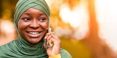 Mobil İletişim. Siyah İslami Kadın 'ın yakın plan portresi, cep telefonuyla konuşan kadın, tesettürlü kadın, keyifli bir telefon görüşmesi, arkadaşla sohbetin keyfi, başka yöne bakan...