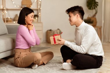 Asyalı Kocanın Mutlu Eşe Paketli Noel Kutusu Vermesi Tatili Kutlaması, Evde Yerde Oturması. Doğum günü ve Yeni Yıl Hediyeleri, Tatil Kutlama Konsepti