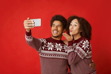 Birbirine aşık çiftlerin selfie 'si. Mutlu Afro-Amerikan erkeği akıllı telefon tutuyor, bayanın öpüşmesi ya da Noel kutlamaları sırasında video araması yapıyor, kırmızı arka planda izole edilmiş, stüdyo çekimi, kopyalama alanı