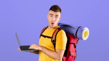 İnternetten turne rezervasyonu. Kamp malzemeleri ve dizüstü bilgisayarı olan genç bir adam online seyahat acentesinde büyük tatil indirimine şaşırdı. Şok olmuş hipster hafta sonu internetten alışveriş yapıyor.