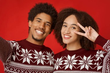Genç bir çiftin Xmas ya da Yeni Yıl 'da çekilmiş aile fotoğrafı. Neşeli Afro-Amerikan erkek ve kadın portresi, elinde barış işareti, kırmızı arka planda izole edilmiş, yakın plan