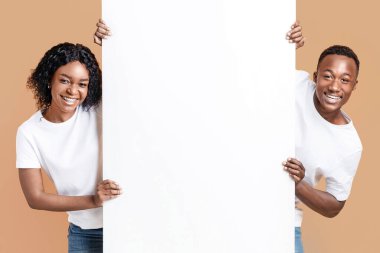 Neşeli Afro-Amerikan çift reklam için boş pano tutuyorlar ya da sarı arka planda mesaj atıyorlar. Gülümseyen siyah adam ve kadın reklam için boş pankartın yanında duruyorlar.