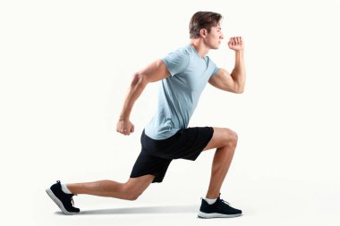 Spor giyim kuşağında ışık stüdyosu arka planında hamleler yapan güçlü bir milenyum erkeğinin yan görüntüsü. Kararlı atletik adam egzersiz yapıyor, bacaklarını esnetiyor ya da antrenmandan önce ısınıyor.