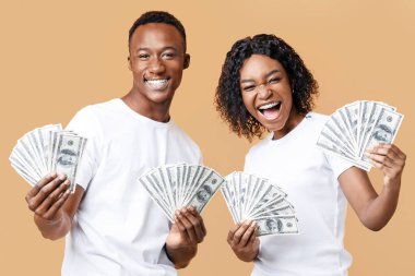 Kumar, kredi konsepti. Neşeli siyah adam ve kadın piyango kazandılar, kameraya ödül gösterdiler ve çığlık attılar. Duygusal Afrikalı-Amerikalı çift ellerinde para destesi tutuyorlar, sarı stüdyo geçmişi var.