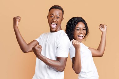 Emotional african american young couple celebrating success on yellow studio background. Happy black man and woman clenching fists and screaming, won the prize or got exciting news