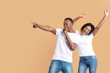 Şarkı söyleyip dans eden pozitif siyah çift sarı stüdyo arka planındaki boşluğu işaret ediyor, panorama. Neşeli genç Afrikalı Amerikalı erkek ve kadın eğleniyor, reklam gösteriyorlar.