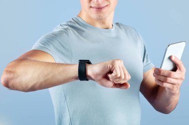 Menekşe stüdyosunun arka planında akıllı ve cep telefonlu genç sporcunun görüntüsü var, elleri yakın. Milenyum sporcusu antrenman sırasında spor izleme verilerini kontrol ediyor.