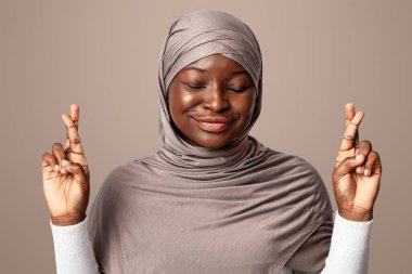 Batıl inançlı, tesettürlü, tesettüre girmiş, parmakları kapalı, gözleri kapalı, gülümseyen, şans dileyen Afrikalı, Müslüman bir kadın.