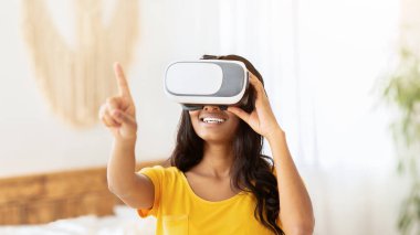 Evde kal. Sanal gerçeklik kulaklığı takmış genç Afrikalı Amerikalı kadın evdeki siber uzayı keşfediyor. VR gözlüklü siyahi kadın içeride interaktif video oyunu oynuyor.