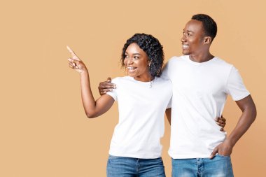 Neşeli siyah kadın sarı stüdyo arka planında erkek arkadaşına fotokopi odasını gösteriyor. Afro-amerikan aşıklar boş alanlara bakıyorlar. Reklamınız veya mesajınız için. Boş alanlı panorama.