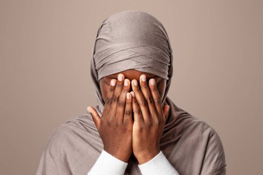 Müslüman Ayrımcılığı Konsepti. El tesettürlü, tesettürlü, korkmuş zenci kadın. Ağlayan, başörtüsü takmış Afrikalı kadının portresi. Işık stüdyosu arka planında duruyor.