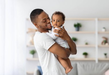 Baba ve Çocuk. Mutlu, genç, siyah bir baba, evde birlikte poz verip, Afrikalı Amerikalı babayı seven, çocuğuna bakan, gülümseyen ve boşluğu kopyalayan tatlı bir erkek çocuğu kucaklıyor.