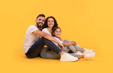 Modern Ortadoğu Ailesi. Mutlu Arap Baba, Anne ve Kız Sarılıyor Birlikte Stüdyoda Otururken Sarı Arkaplanda. Aileler ve çocukları kameraya gülümsüyor
