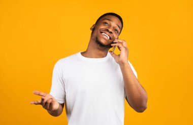 Cep telefonuyla konuşan pozitif Afrikalı adam sarı arka planda duruyor. Stüdyo Çekimi