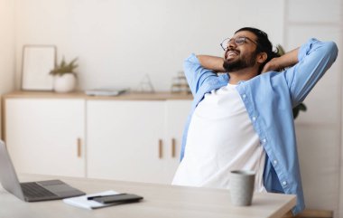Neşeli Arap serbest çalışanı, başarılı bir işten sonra arkasını yaslıyor, bilgisayarlı masada oturuyor, Millennial Man, elleri başının arkasında işyerinde dinleniyor.