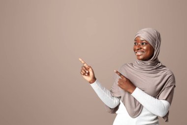 Şuraya bak. Türbanlı Mutlu Siyahi Kadın Teklif ya da Reklamınız İçin Bedava Yer Gösteren İki Elli Afro Müslüman Kadın, Kopya Boşluğu 'nu Gösteriyor.