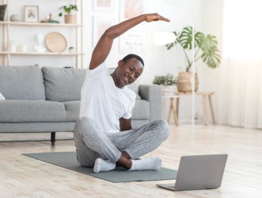 Spor dersleri çevrimiçi. Genç siyah adam evde geriniyor, dizüstü bilgisayar kullanıyor, boşluğu kopyalıyor.