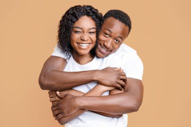 Stüdyonun arka planında sarılıp yatan sevimli siyah çift. Neşeli genç Afro-Amerikan erkek ve kadın kameraya sarılıp gülümsüyor. Aşk, ilişkiler, evlilik kavramı