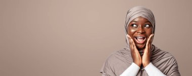 Vay canına, harika bir teklif. Şok olmuş Afrikalı Müslüman kadın tesettüre bakıyor, heyecanla kopyaya bakıyor, siyah İslamcı kadın yüzüne dokunuyor ve hayretle haykırıyor, ışığın altında duruyor, panorama