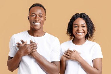 Minnettar Afro-Amerikalı çift her iki avuçlarını göğsünde tutuyor ve gülümsüyor, minnettarlıklarını ve iyi hislerini dile getiriyorlar, sarı stüdyo geçmişi. Mutlu siyah adam ve kadın daha iyisini umuyor.