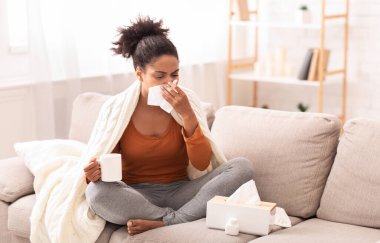 Mevsimsel grip. Hasta Afro Kadın, kağıt mendile burnunu sümkürdü. Evdeki koltukta oturduğu için kötü hissediyordu. Boşluğu Kopyala