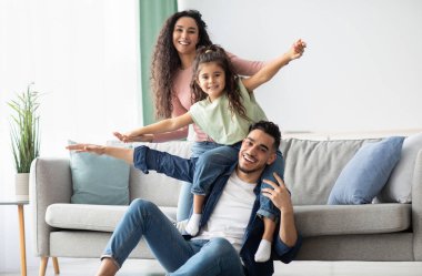 Portrait Of Happy Middle Eastern Parents Bonding With Their Child At Home, Happy Arab Family With Daughter Having Fun In Living Room, Playing And Laughing, Enjoying Spending Time Together, Free Space